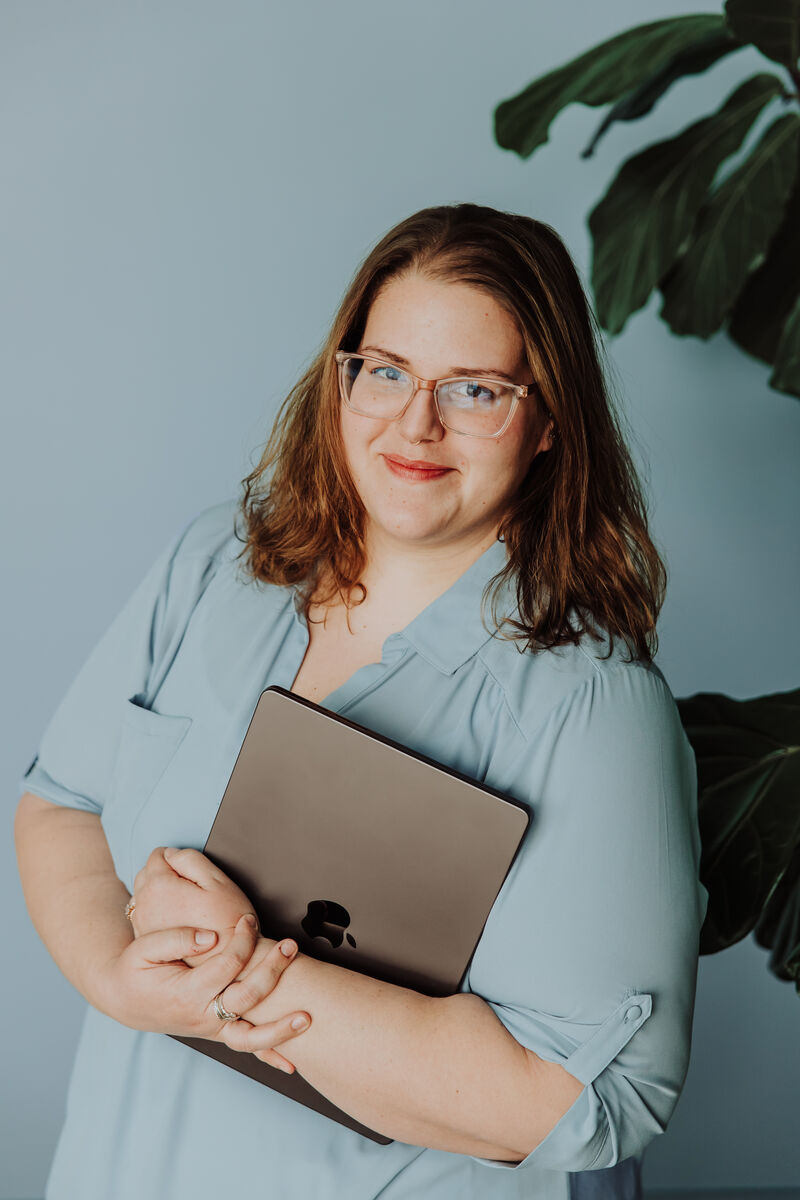Jenn McGeehan standing and smiling, holding her closed laptop