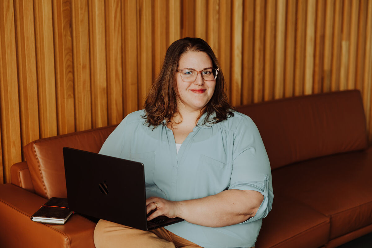 Jenn on a leather couch with a notebook and laptop, smiling