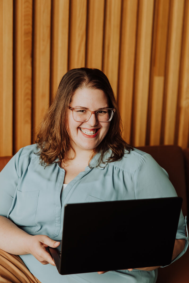 Jenn laughing, holding her open laptop on a leather couch